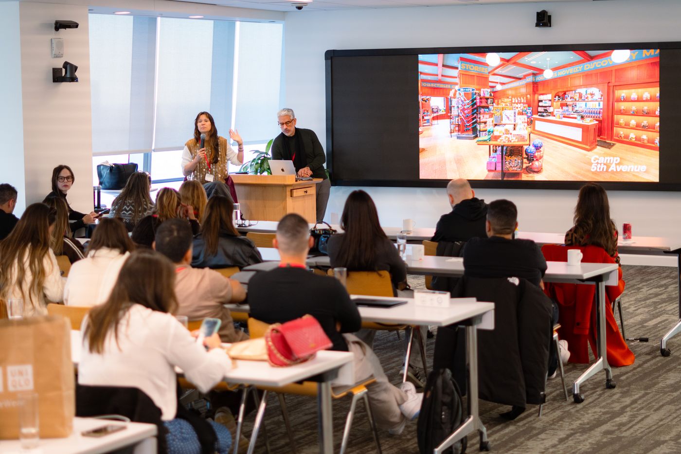Grupo da delegação Brasil Varejo em palestra na NRF, com tela mostrando a loja Camp 5th Avenue